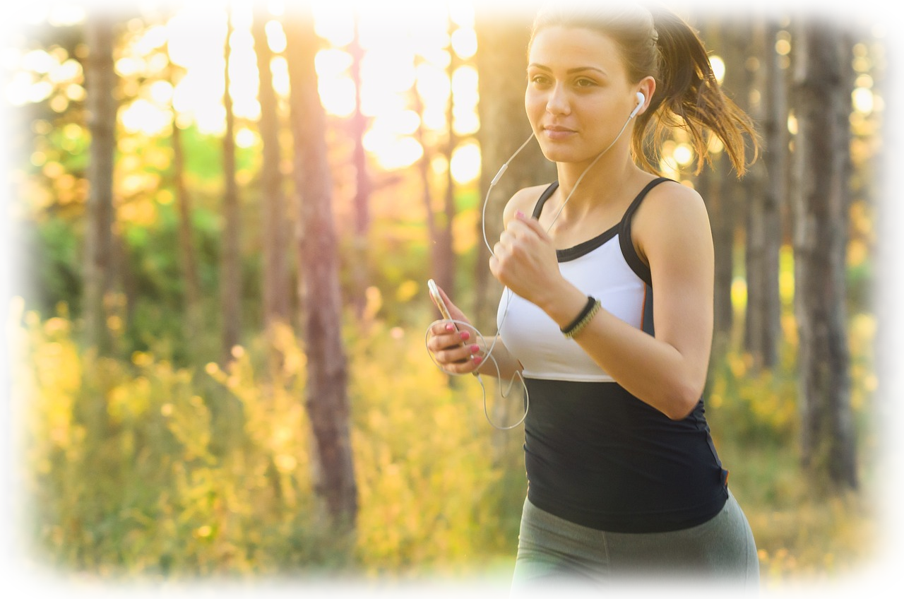 Immagine di una donna che corre all'aperto in un bosco, con le cuffie, godendo della luce del sole al tramonto. Un esempio di esercizio fisico per migliorare energia e benessere.